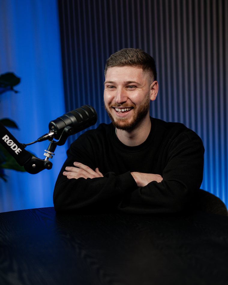 Jackson Morton seated at the studio table with his arms folded, smiling, a microphone in front of him.